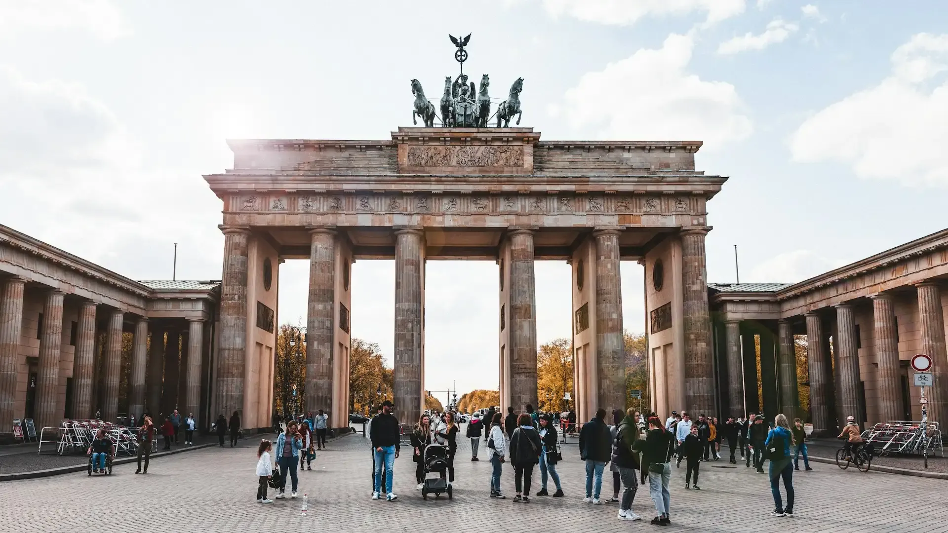 A large stone arch with columns and statues on top with Brandenburg Gate in the background